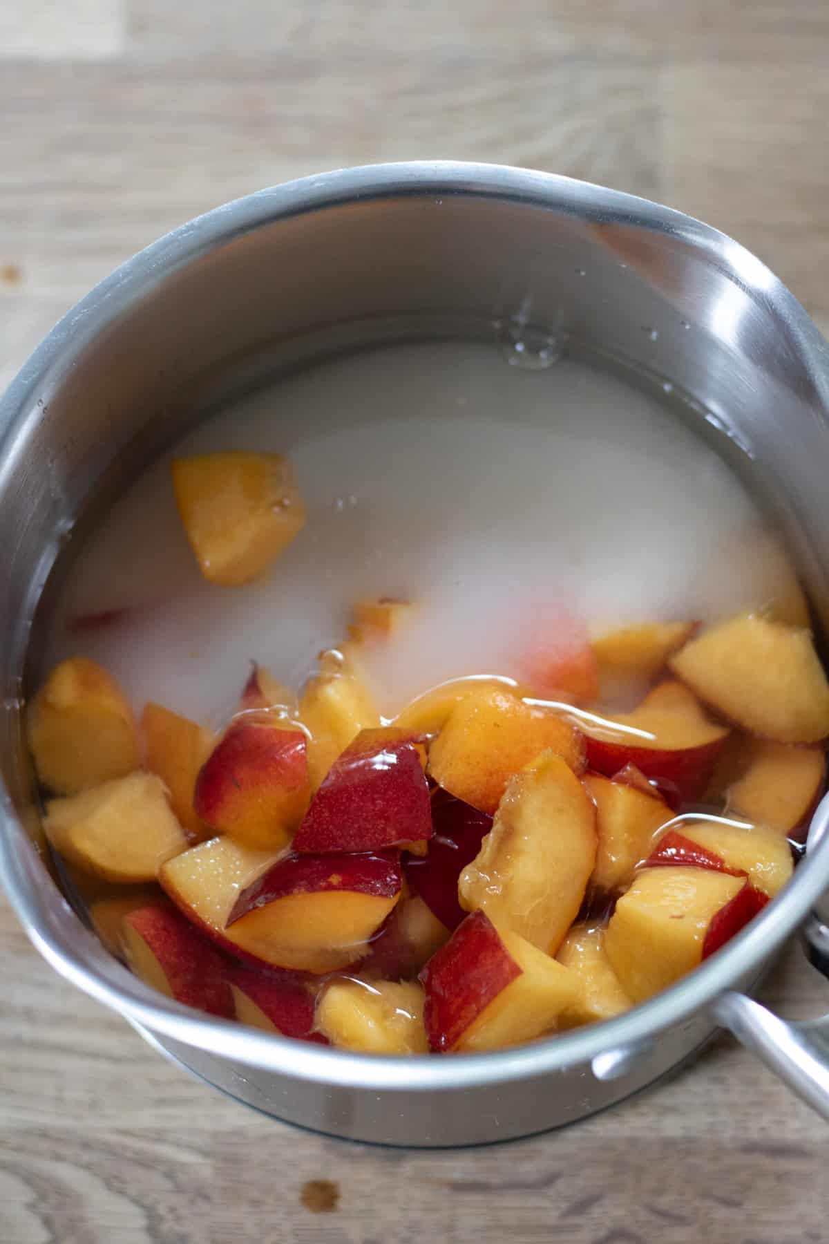 A pot with chopped nectarines, sugar and water.
