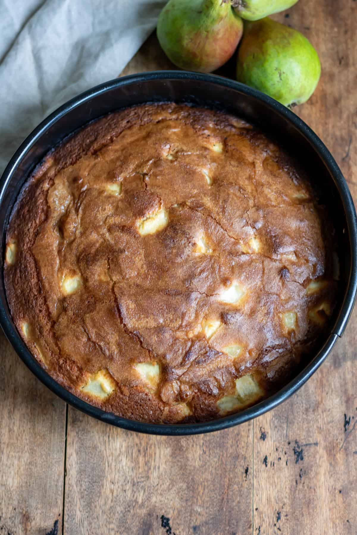 Baked pear cake in a pan on a wooden table.