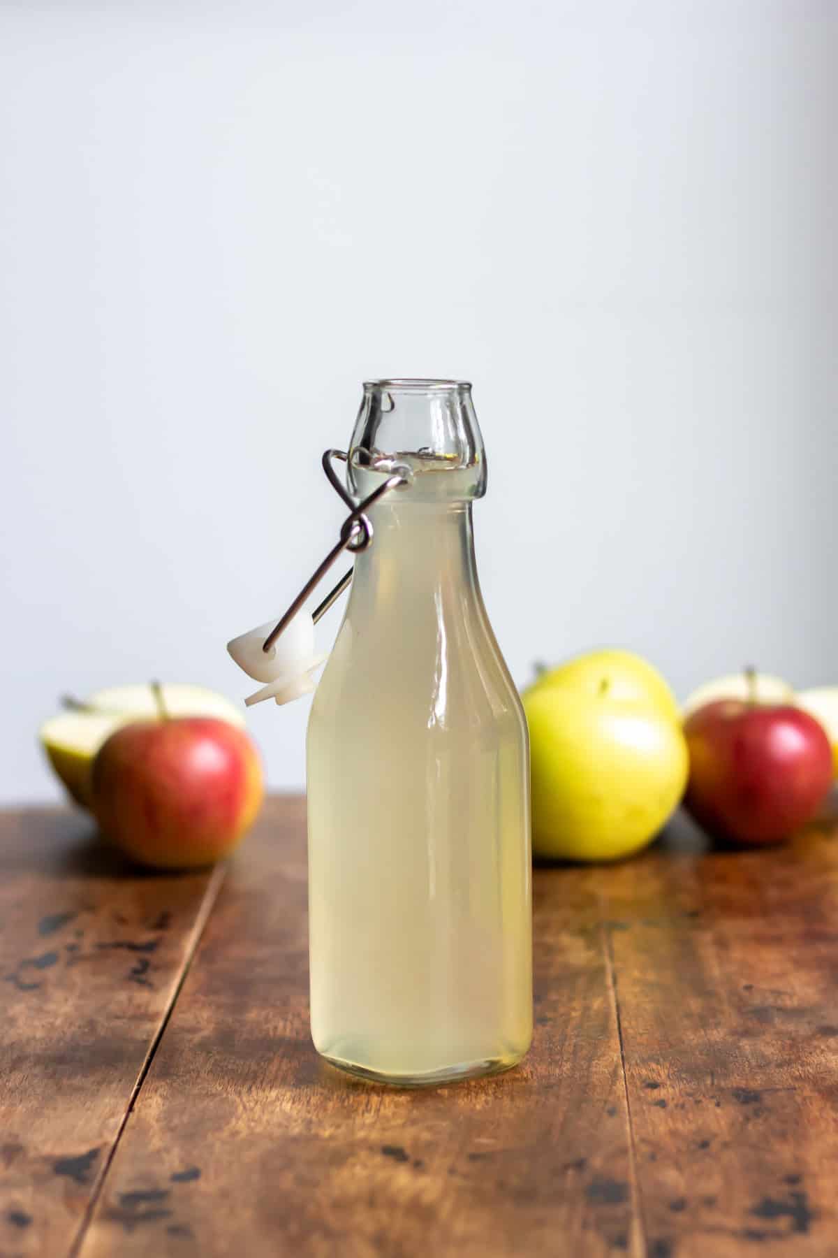 Wooden table with a glass bottle of apple syrup in front of apples.