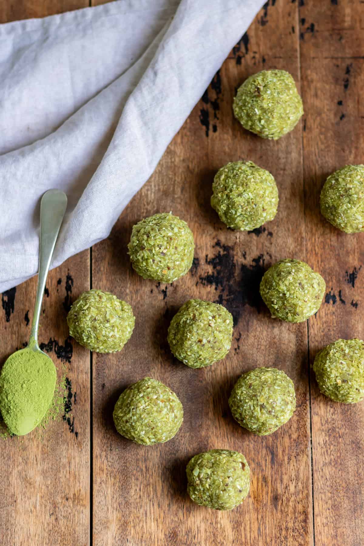 Wooden table with rows of matcha balls and a teaspoon of matcha green tea powder.