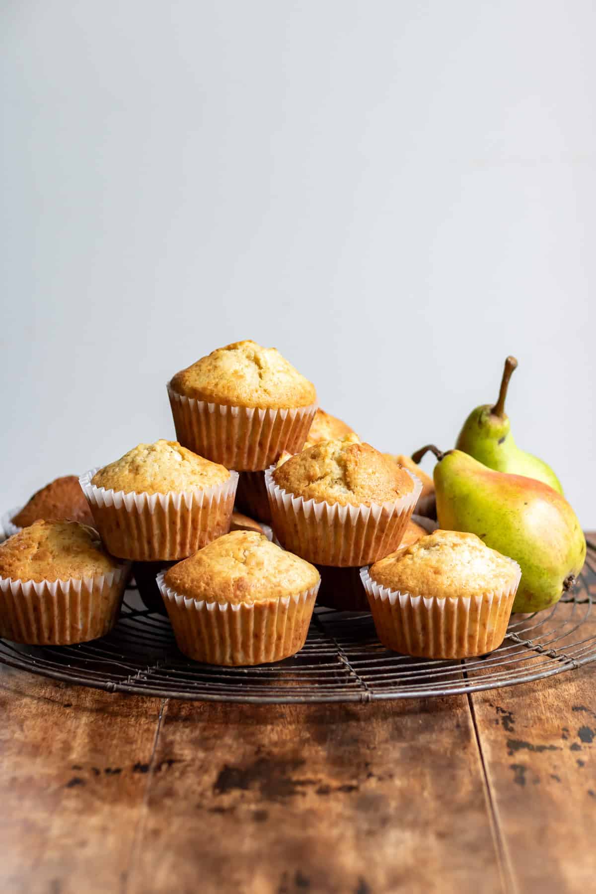 A stack of pear muffins on a wire rack next to fresh pears.