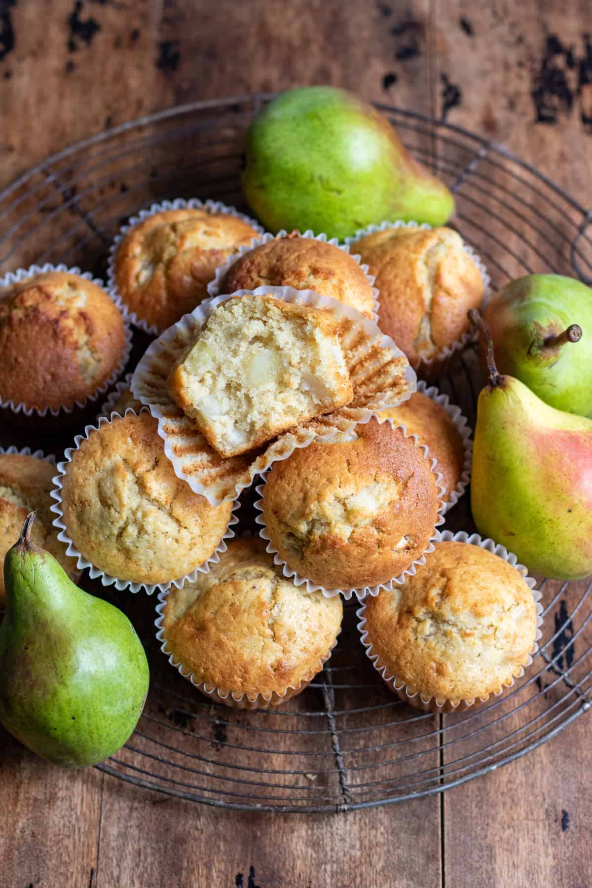 Looking down at a wooden table with a wire rack covered in pear muffins, with one at the top with a bite out.