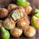 Looking down at a wooden table with a wire rack covered in pear muffins, with one at the top with a bite out.