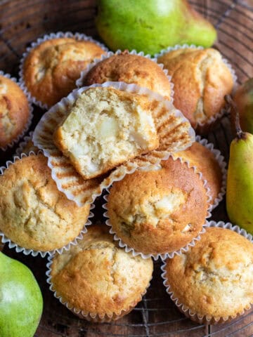 Looking down at a wooden table with a wire rack covered in pear muffins, with one at the top with a bite out.