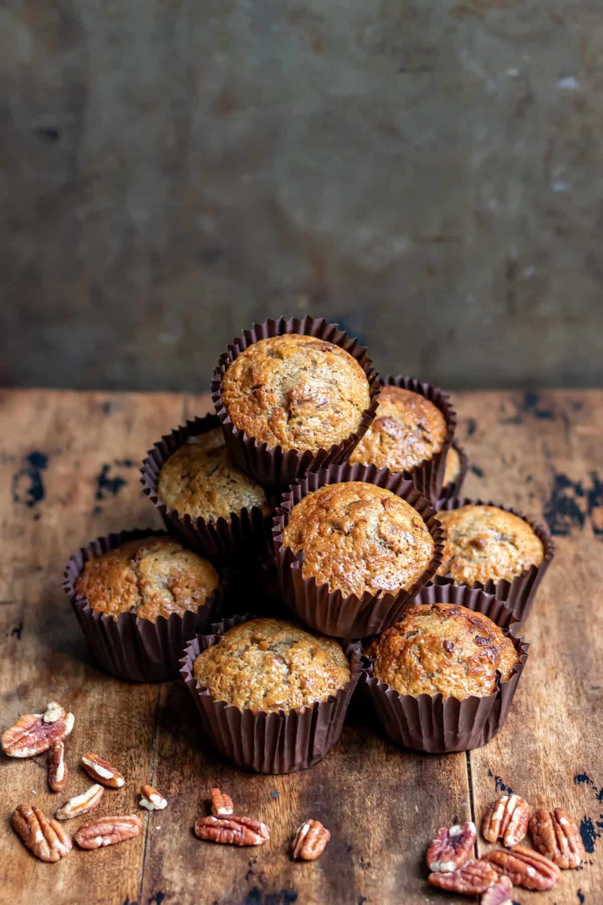 A stack of pecan date muffins on a wooden table with pecans scattered around.