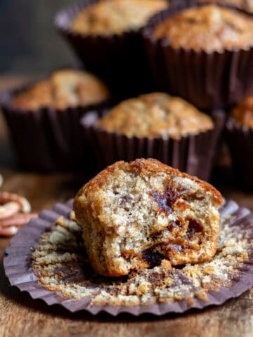 A pecan date muffin with a bite out in front of more muffins.