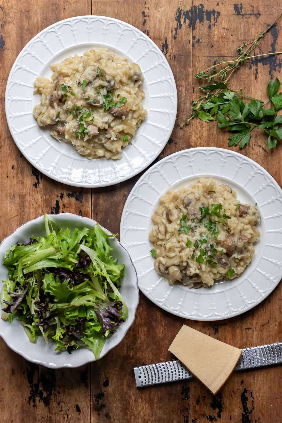 Wooden table with two plates of slow cooker mushroom risotto and a dish of salad.