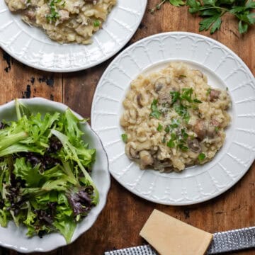 Wooden table with two plates of slow cooker mushroom risotto and a dish of salad.