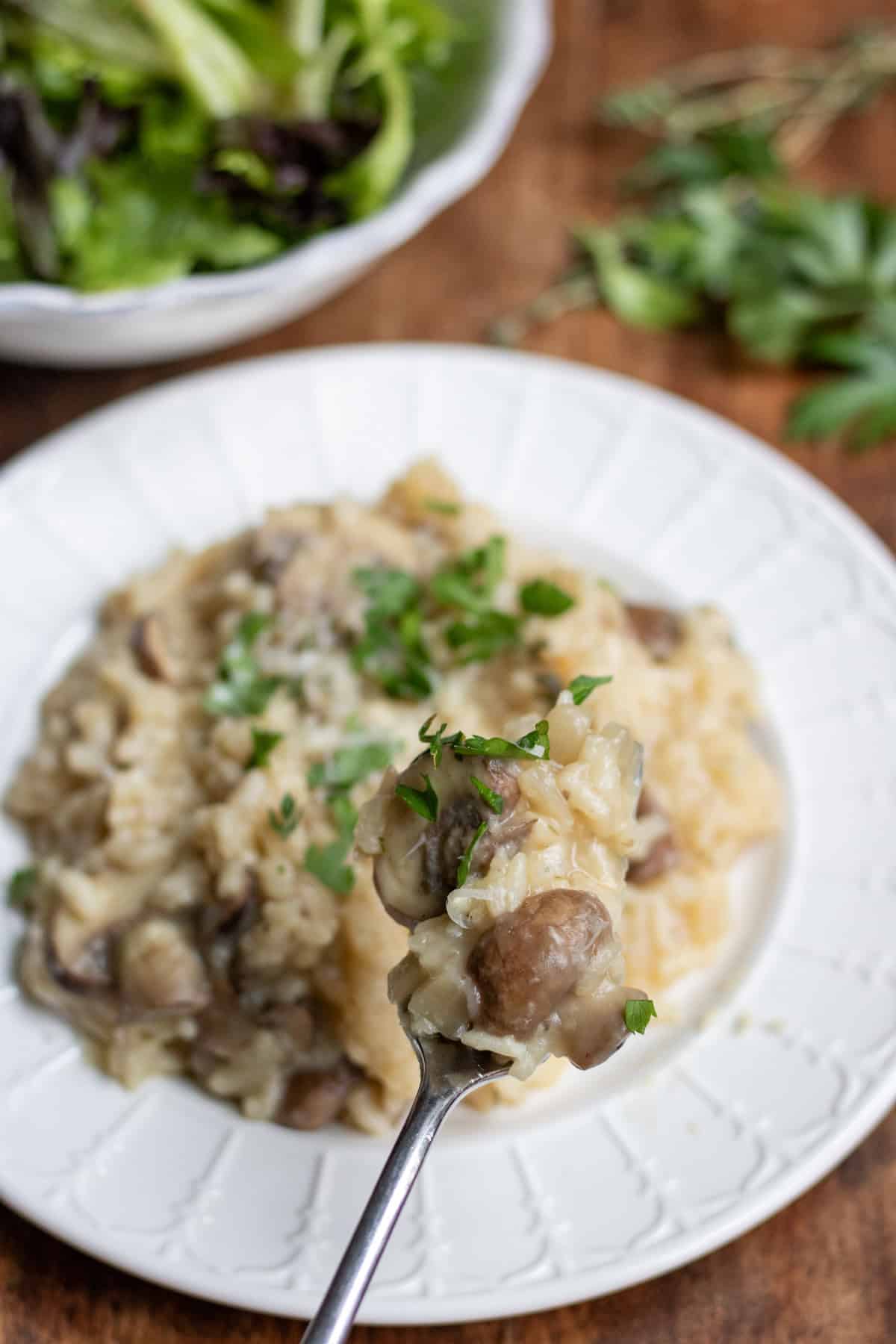 Forkful of slow cooker mushroom risotto in front of the plate of it.
