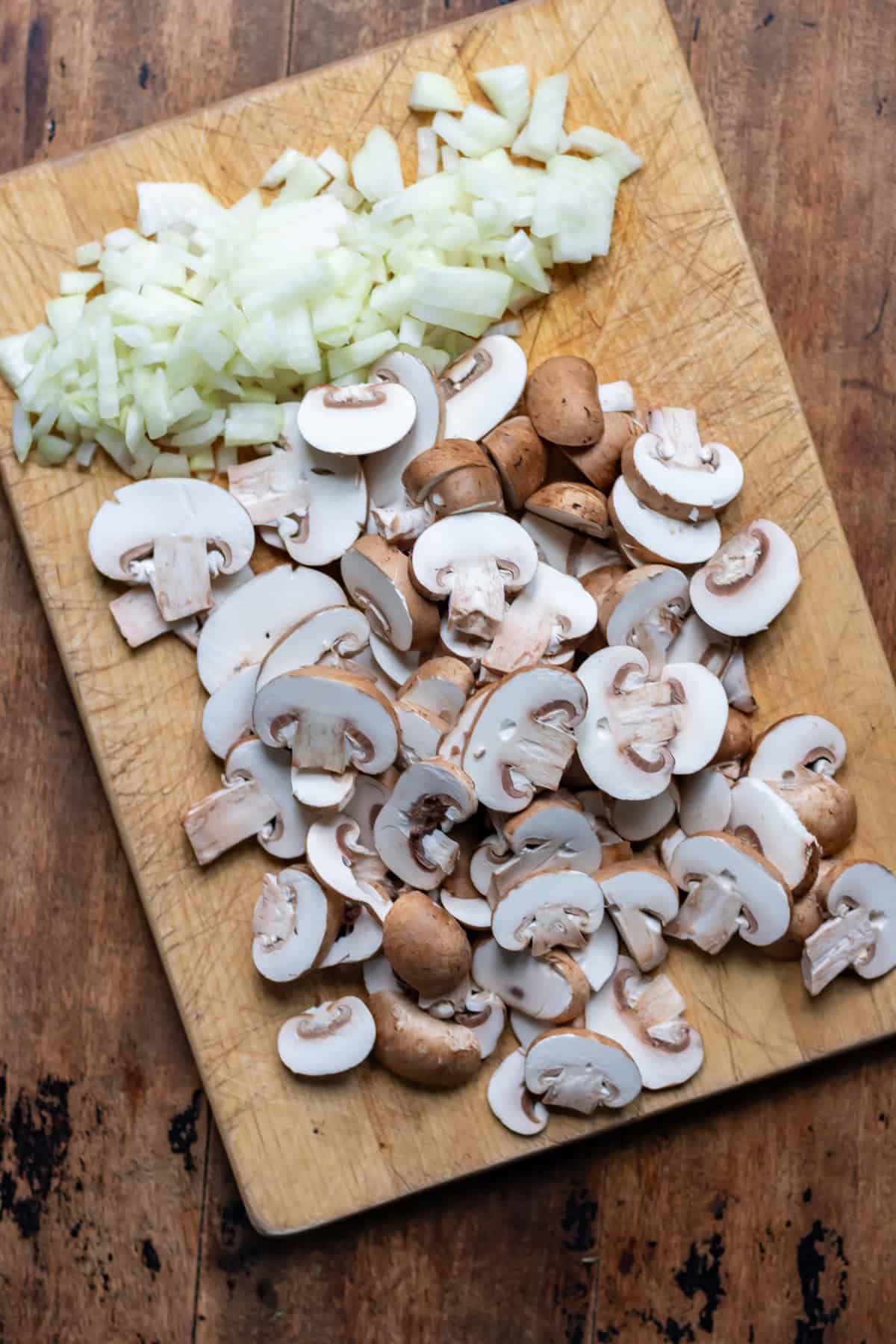 Sliced mushrooms and onions on a wooden cutting board.