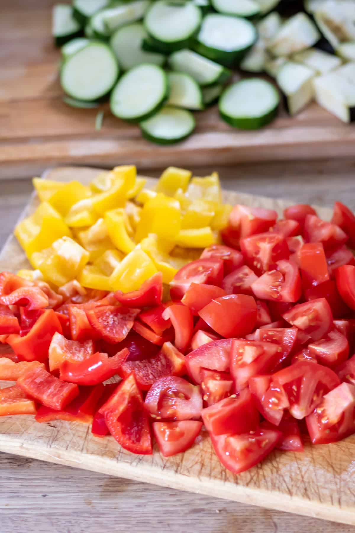 Chopped yellow peppers, red peppers and tomatoes on a cutting board.