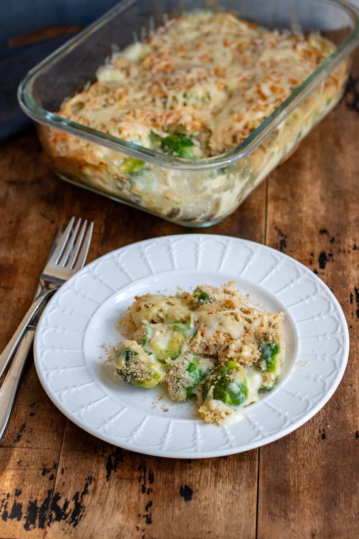 A plate of brussels sprouts au gratin in front of the baking dish of it.