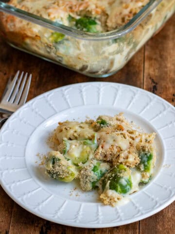 A plate of brussels sprouts au gratin in front of the baking dish of it.