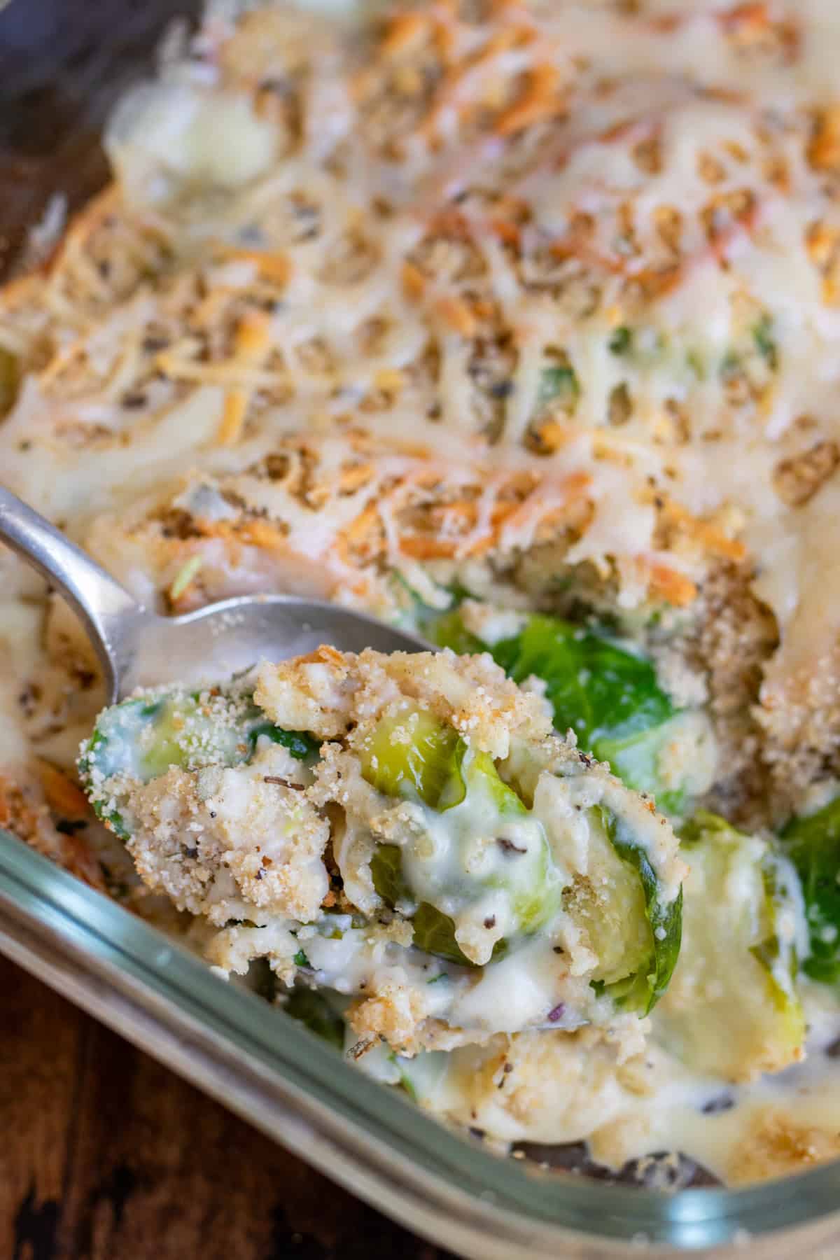 A serving spoon taking a serving of brussels sprouts au gratin from the baking dish..