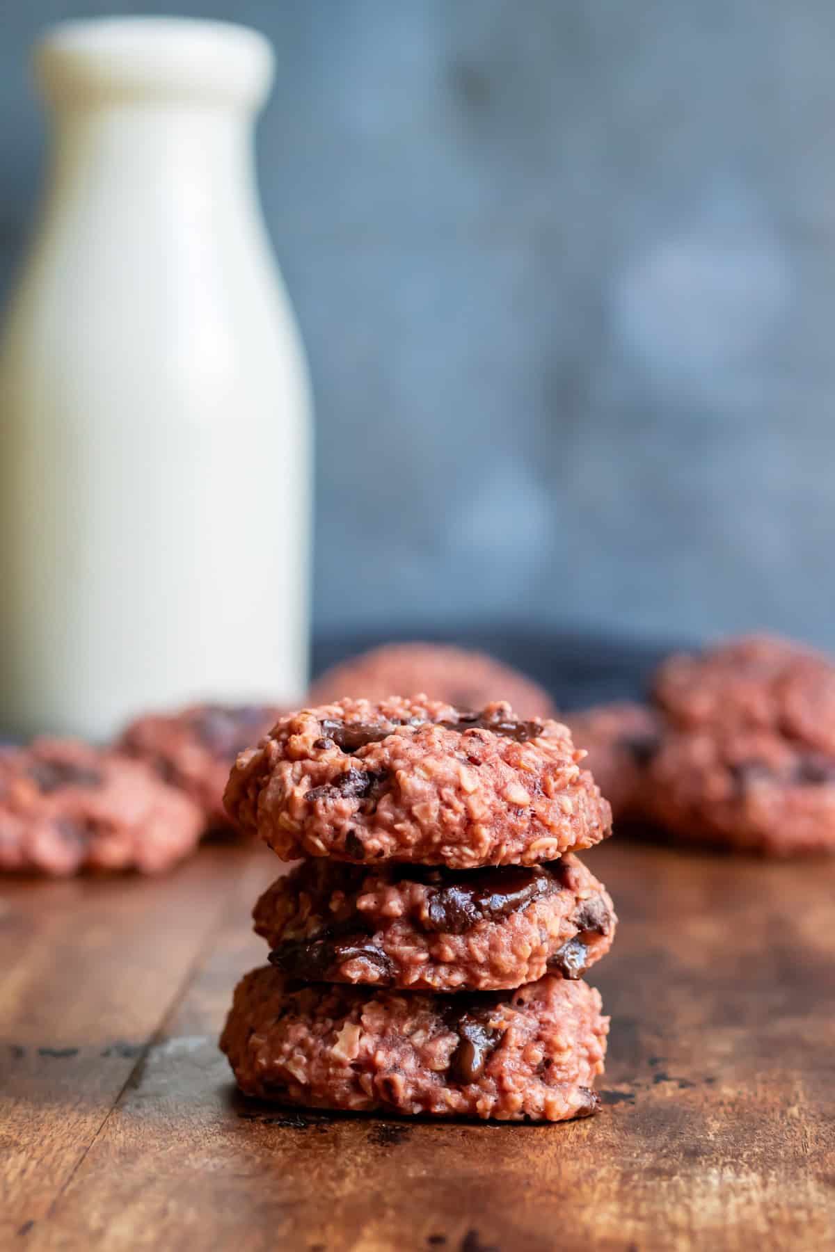 A wooden table with a milk bottle and chocolate chunk beetroot cookies.