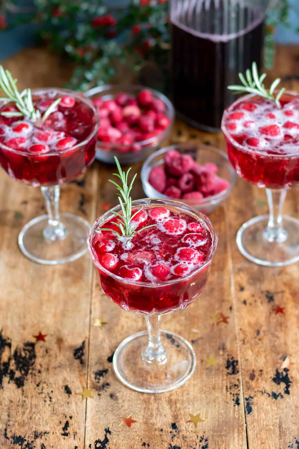 A table with champagne glasses of mulled wine spritzer with frozen cranberries and raspberries and a sprig of rosemary.