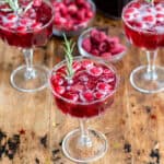 A table with champagne glasses of mulled wine spritzer with frozen cranberries and raspberries and a sprig of rosemary.