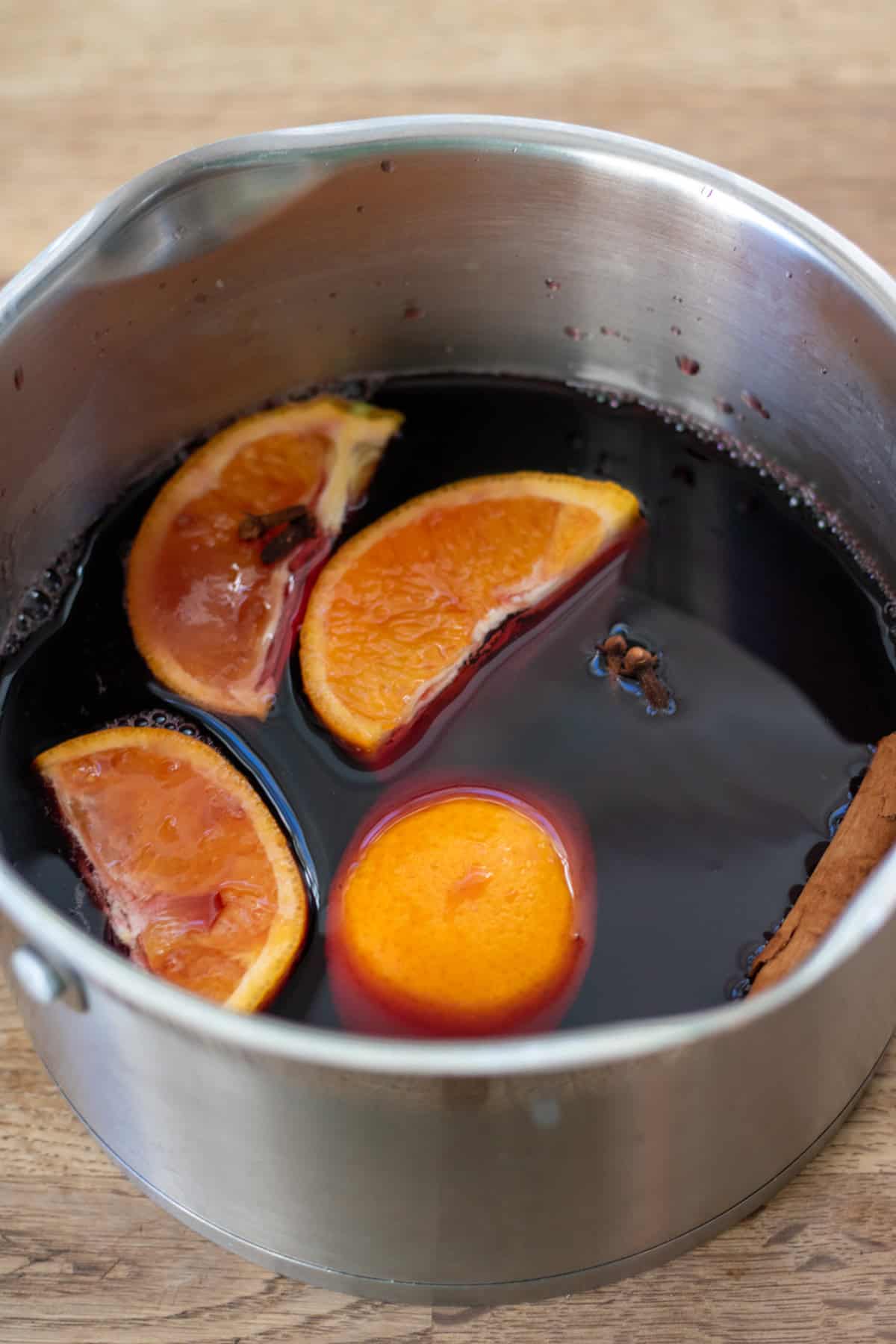 Red wine, quartered orange, cinnamon stick, cloves and brown sugar in a pot.