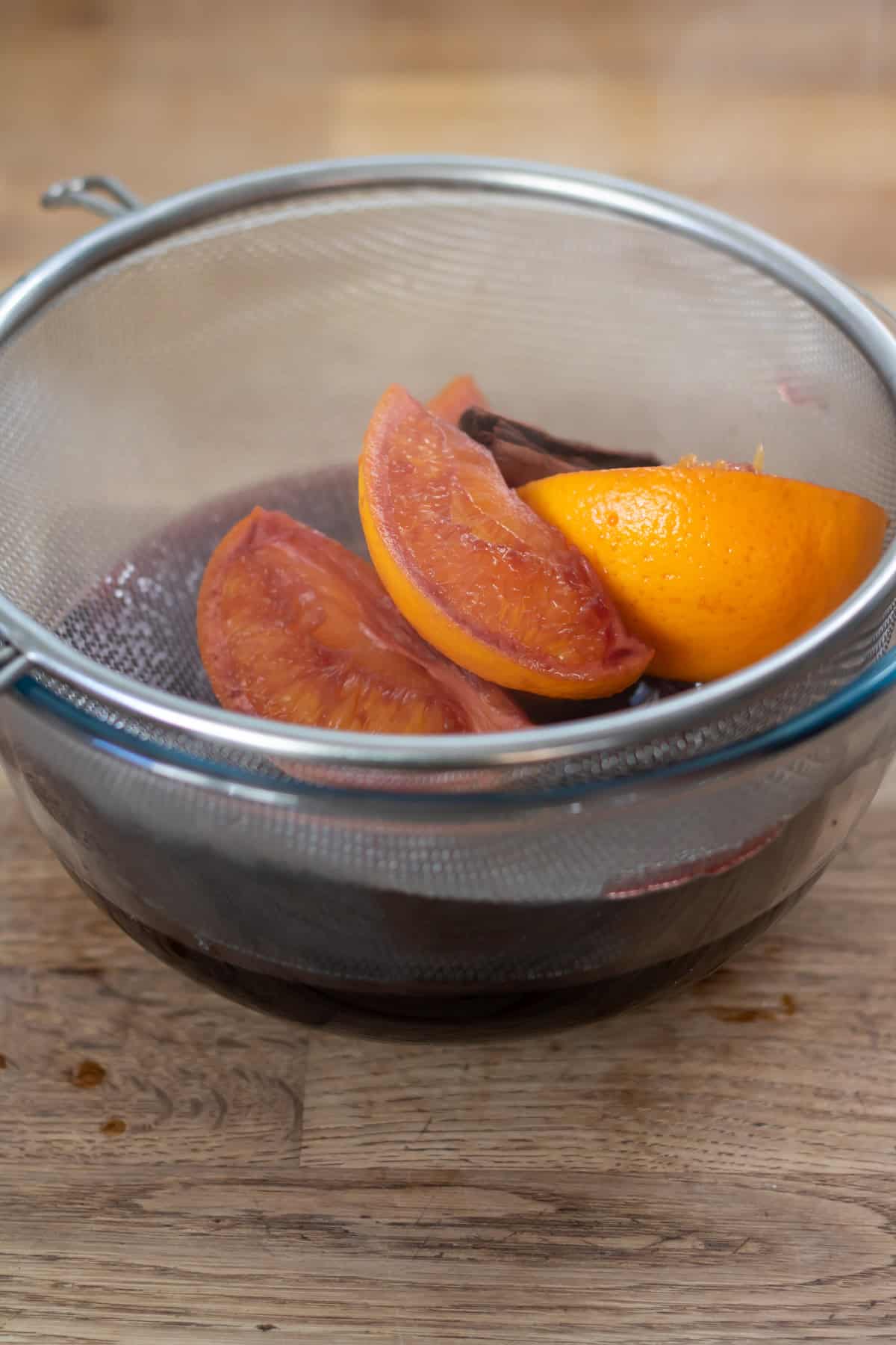 Straining the oranges and spices out of the mulled wine over a bowl.