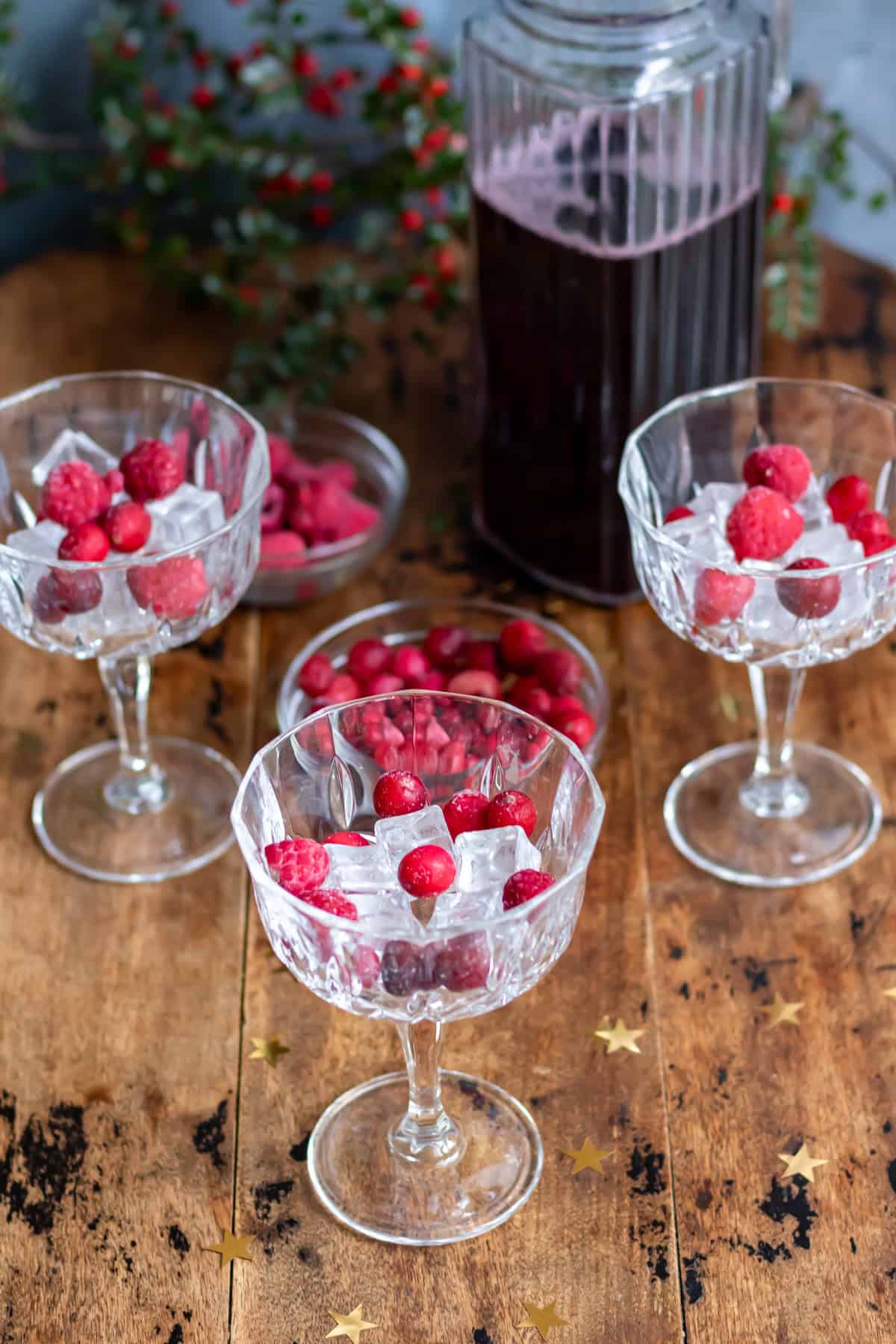 Champagne coupes with ice, frozen cranberries and frozen raspberries.