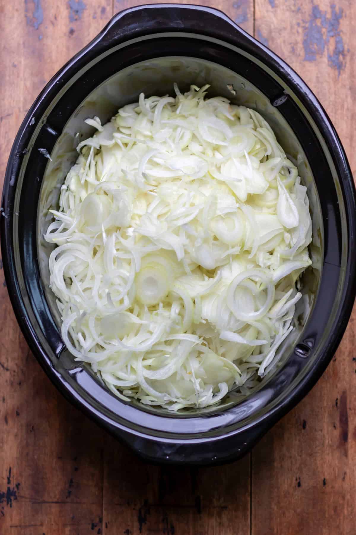 Sliced onions in the bowl of the slow cooker.