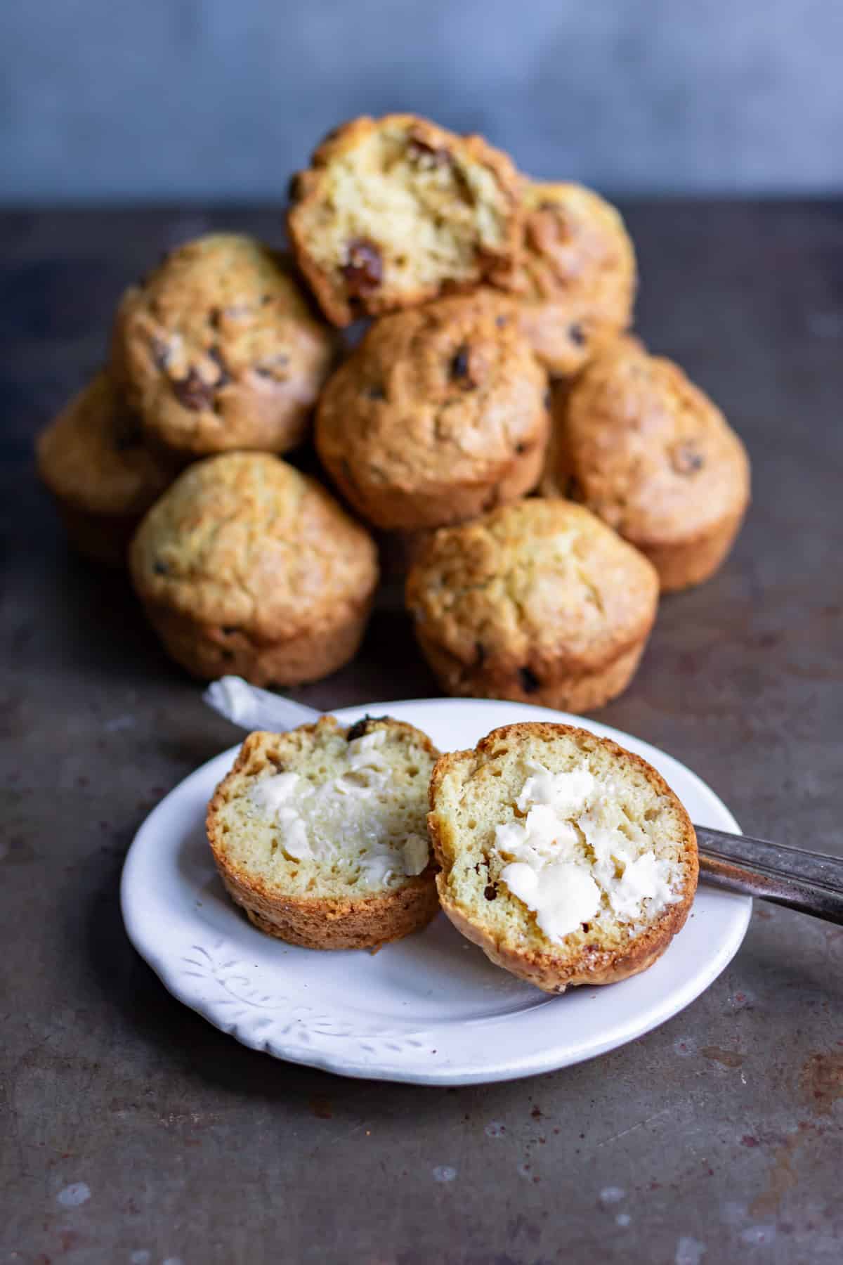 A plate with a buttered soda bread muffin in front of a pile of them.