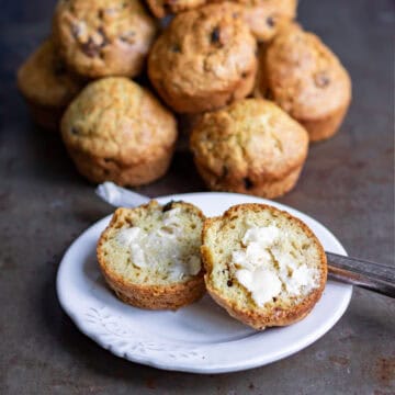 A plate with a buttered soda bread muffin in front of a pile of them.