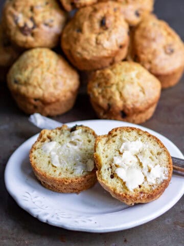 A plate with a buttered soda bread muffin in front of a pile of them.