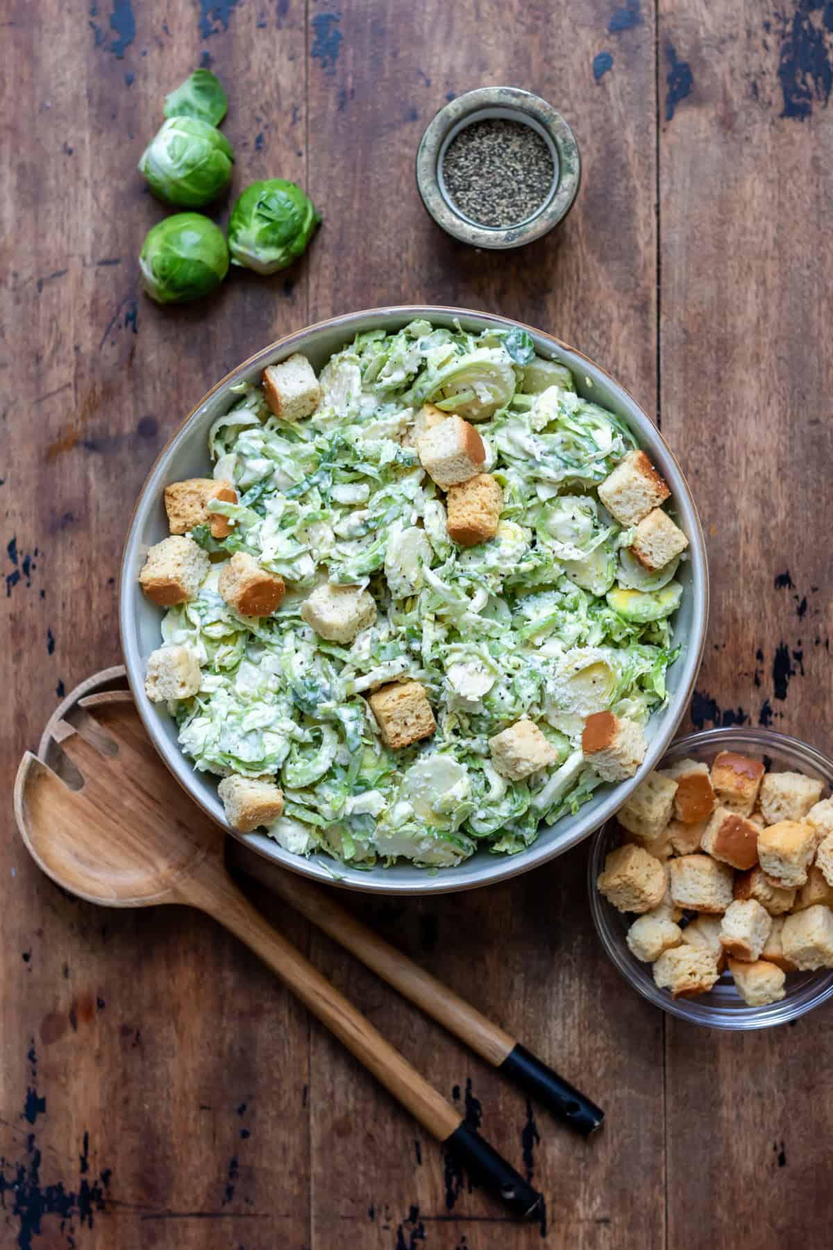 Wooden table with a bowl of brussels sprouts caesar slaw.