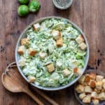 Wooden table with a bowl of brussels sprouts caesar slaw.