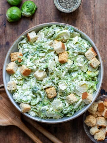 Wooden table with a bowl of brussels sprouts caesar slaw.