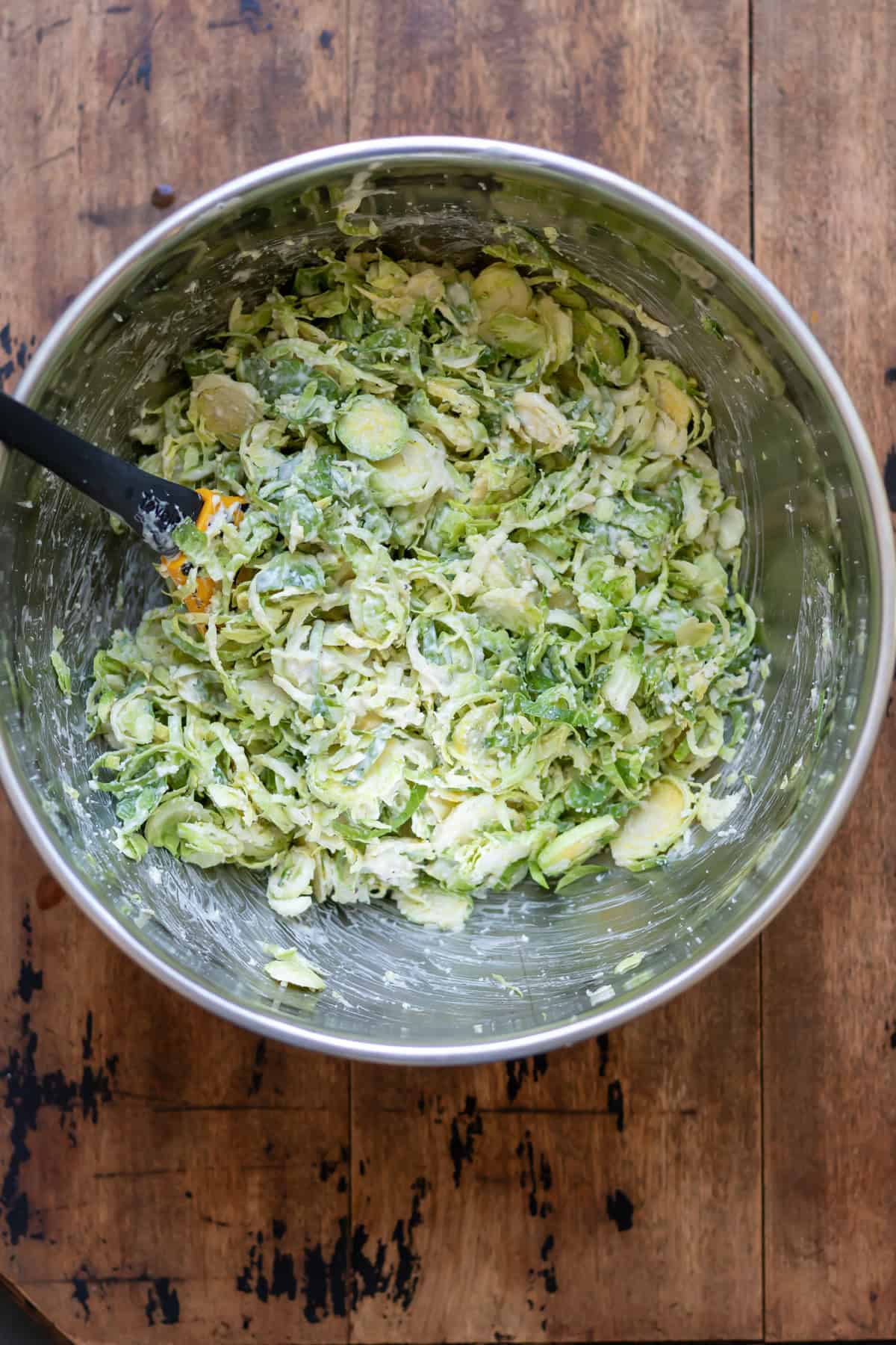 Mixing the shredded brussels sprouts, caesar dressing and parmesan in a bowl.