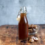 Bottle of chestnut simple syrup on a wooden table next to chestnuts.