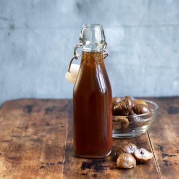 Bottle of chestnut simple syrup on a wooden table next to chestnuts.