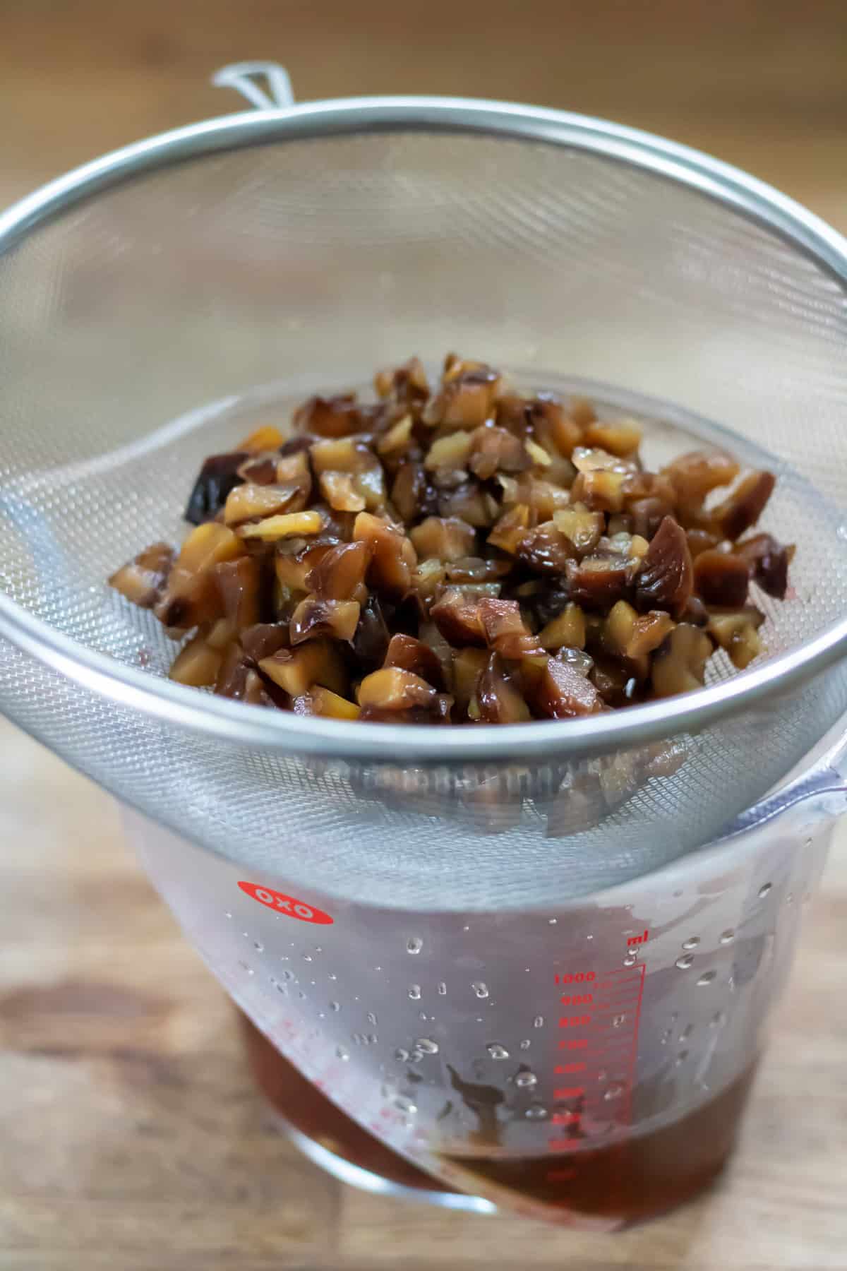 Straining the chestnuts out of the chestnut syrup in a strainer over a bowl.