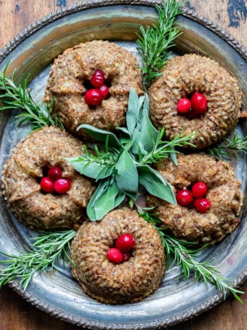 A serving platter with mini bundt chestnut roasts surrounded by fresh herbs and cranberries.