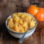 Side view of a dish of persimmon compote next to a few persimmons.
