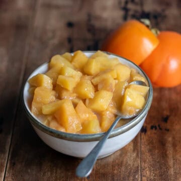 Side view of a dish of persimmon compote next to a few persimmons.