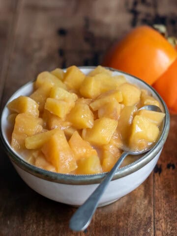 Side view of a dish of persimmon compote next to a few persimmons.
