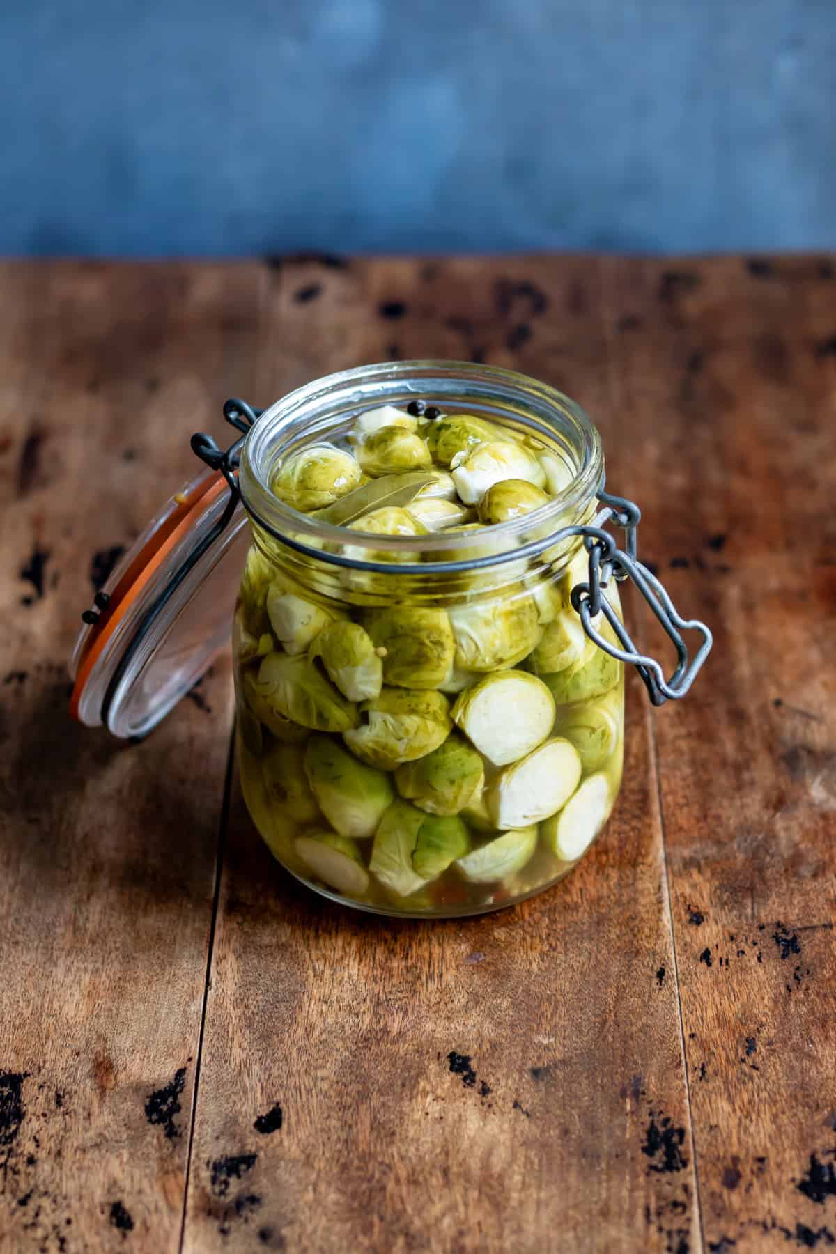 A wooden table with a glass jar of quick pickled brussels sprouts.