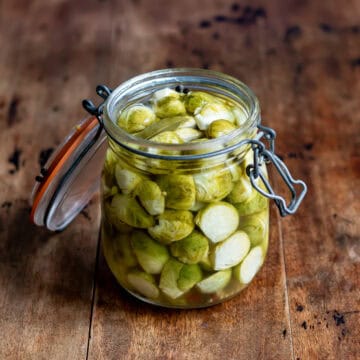 A wooden table with a glass jar of quick pickled brussels sprouts.