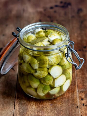 A wooden table with a glass jar of quick pickled brussels sprouts.