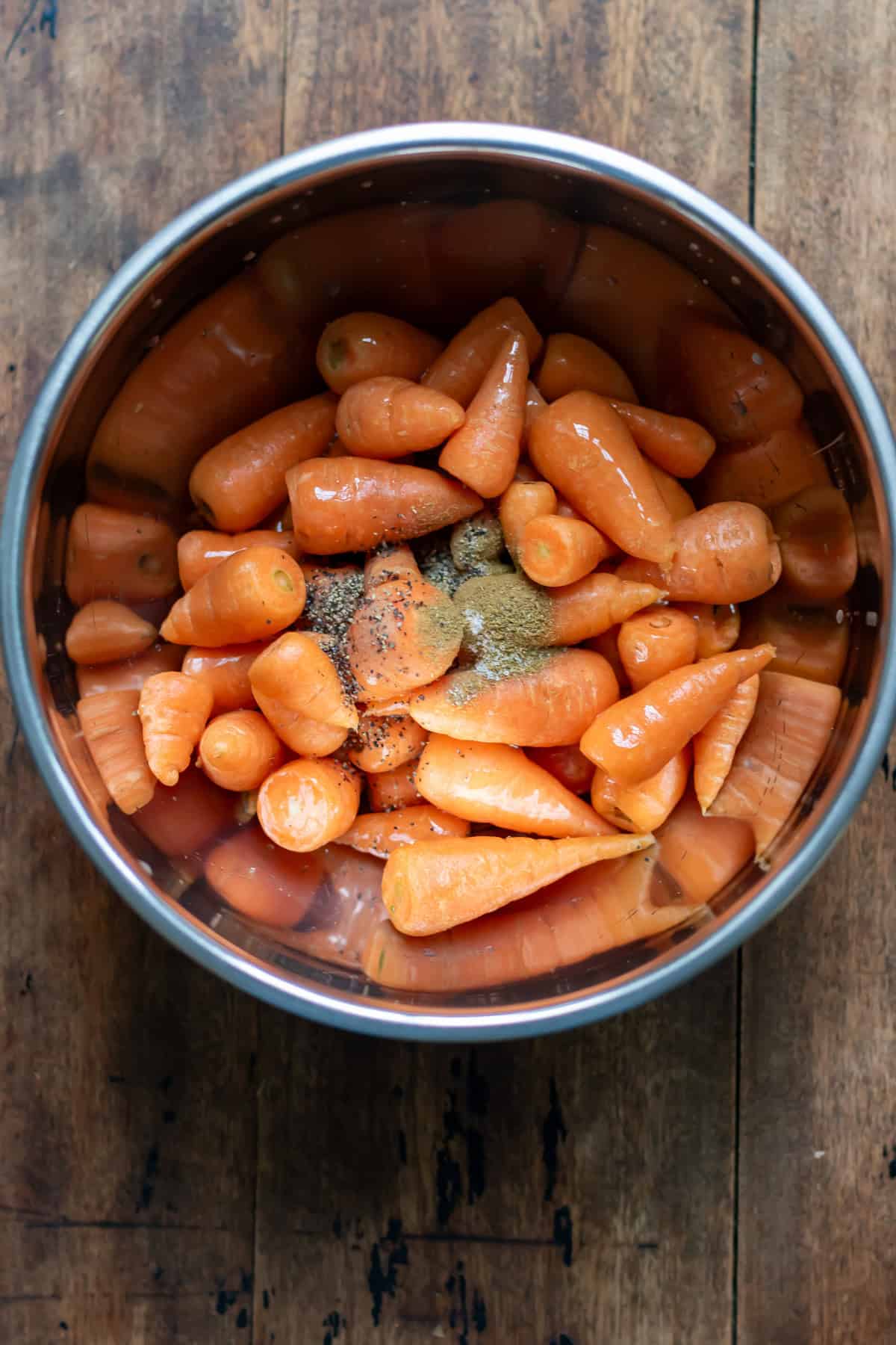 Carrots, oil, cumin, salt and pepper in a bowl.