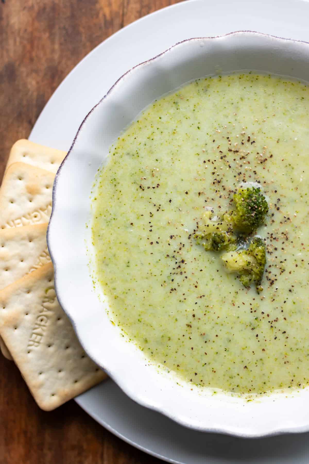 Close up of a bowl of blended broccoli soup with some crackers next to it.