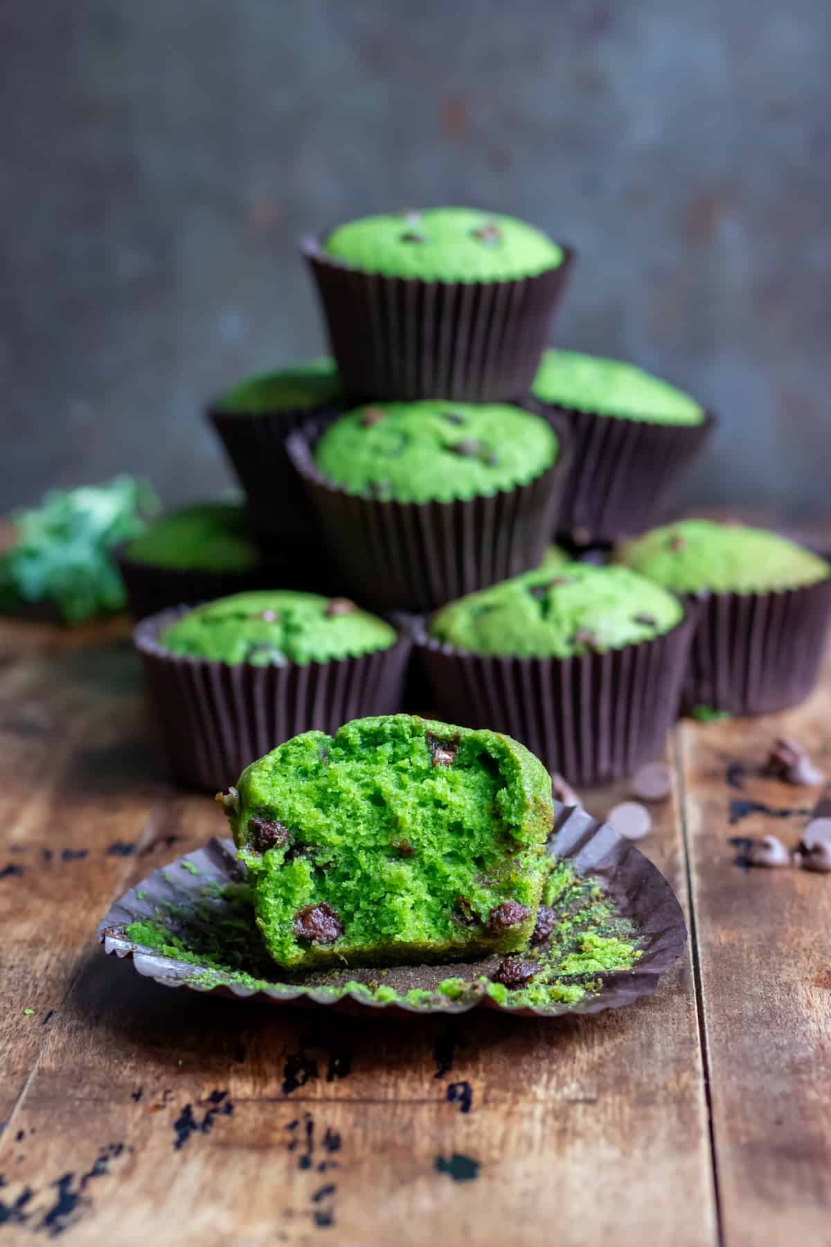A chocolate chip kale muffin with a bite out, in front of a pile of muffins.