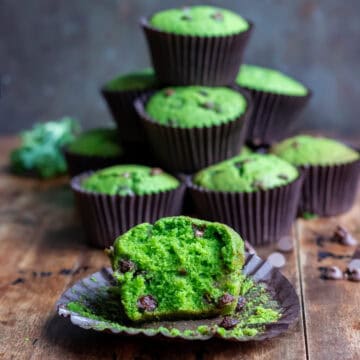 A chocolate chip kale muffin with a bite out, in front of a pile of muffins.