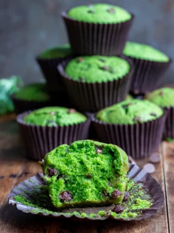 A chocolate chip kale muffin with a bite out, in front of a pile of muffins.