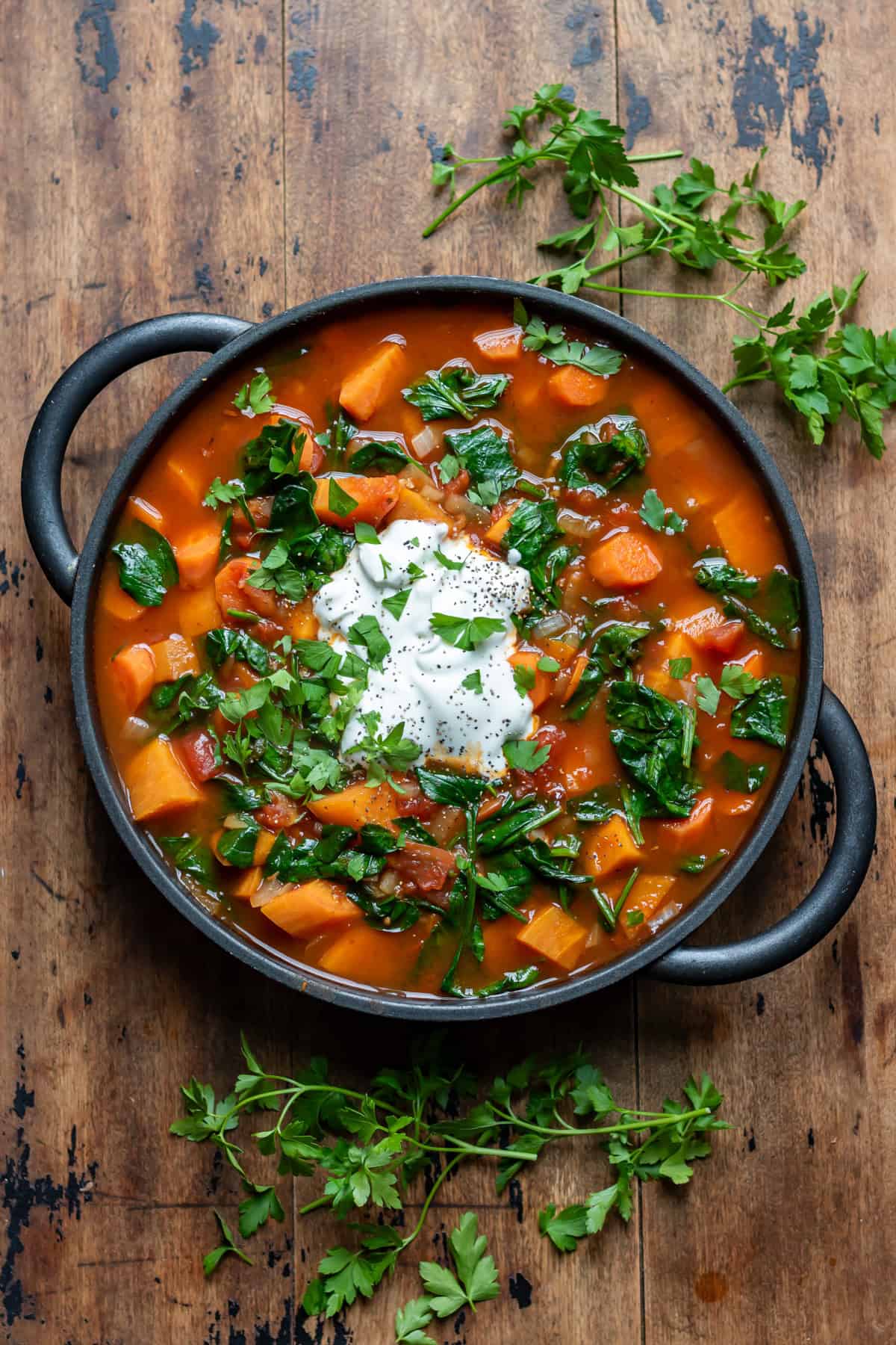 Wooden table with a serving dish of chipotle sweet potato soup topped with yogurt and herbs.
