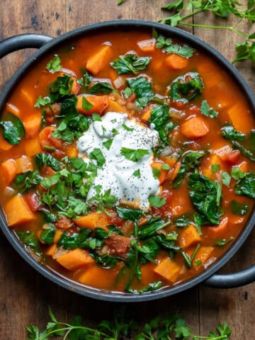 Serving dish of chipotle sweet potato soup with a dollop of yogurt and sprinkled with herbs.