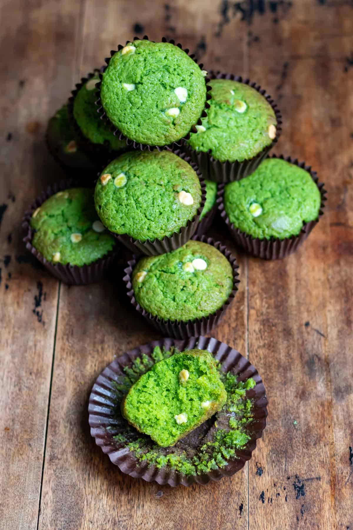 Wooden table with a pile of lemon spinach muffins, with one in front with a bite out.